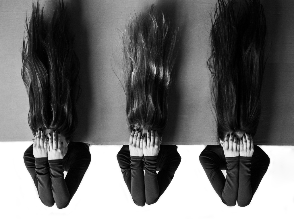 A monochromatic photo of three women - all with long hair - lying on the edge of a concrete platform, their hands covering their faces. The special thing about this photo is that the image has been rotated 180 degrees so that their hair flows upwards.