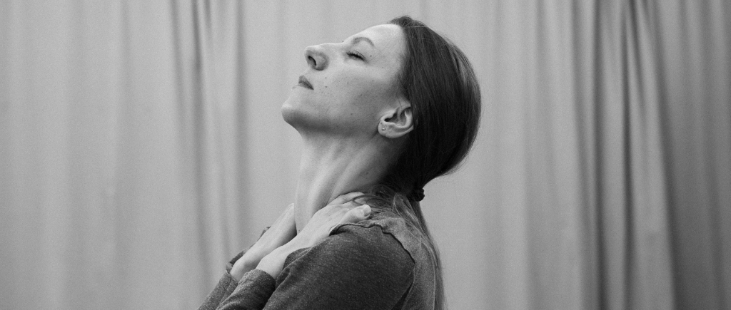 Nina Bulgakova in the rehearsal room. She grips her shoulders with her face raised upwards, eyes closed.