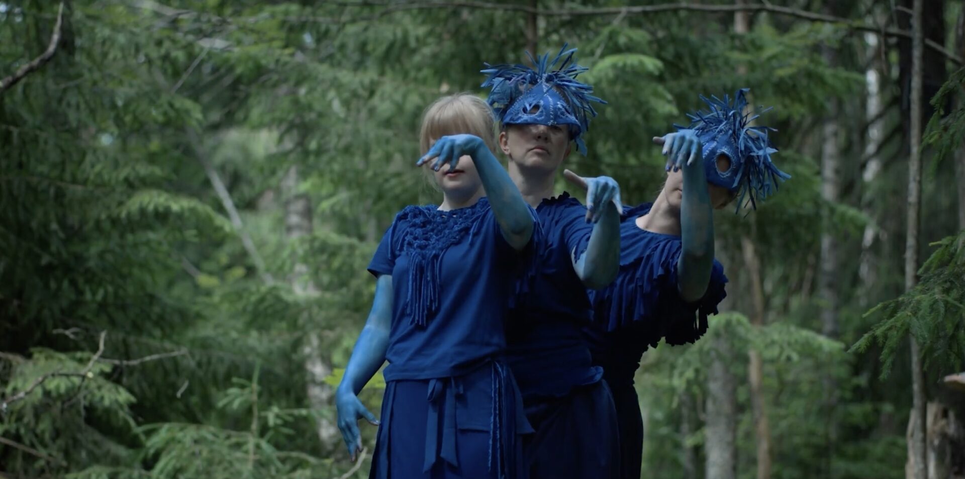 Three young dancers in rich blue costumes are dancing in the forest