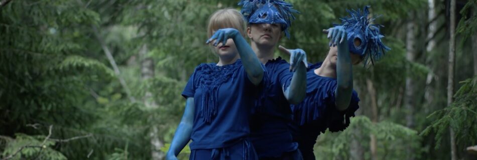 Three young dancers in rich blue costumes are dancing in the forest